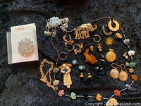 All jewelry pieces on dark fabric showing variety of pins, earrings, brooches, and necklaces including holiday brooch packaging