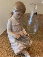 Front angle of seated girl figurine holding chalkboard marked ABC with crystal vase behind it