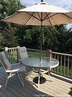 Full view of the outdoor patio table with beige umbrella and two cushioned folding chairs on deck.