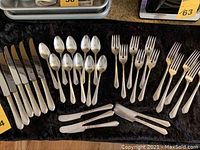 Full set overview of 33 pieces of flatware including knives, forks, spoons, and butter knives laid out on a black cloth.