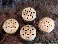 Top view of four sterling silver salt and pepper shakers with varied hole patterns on tops showing wear and tarnish.