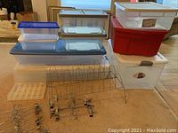 Full view of various sizes of plastic storage bins stacked and placed on floor, metal shoe rack placed horizontally in front of bins, and several metal pant hangers with clips scattered in front.