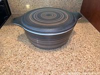 Whole view of the casserole dish with cover, showing the Terra pattern of concentric circles in brown and tan with two handles.