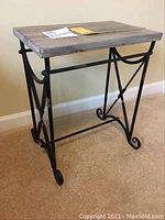 Side view of the table showing iron black metal decorative base with scroll detailing and wooden top with natural finish.