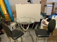 Full view of round glass top table and two bar stools in storage area