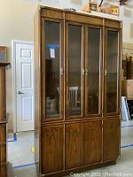 Front view of the tall wood china cabinet showing four glass doors and wooden lower doors.