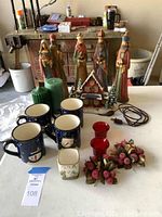 Full overview of the lot including Nativity figures, snowman mugs, lighted house, candles, and candle rings on table with background showing workshop items.