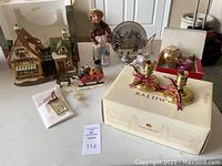 Full lot view showing Baldwin candle sticks on their box, a lighted house, decorative plate, assorted Christmas ornaments including a gold ornament ball, and a small Santa figurine with a sleigh.