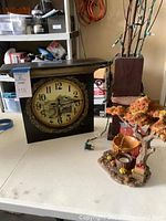 Photo shows black wood clock with hand-painted face, square shape, placed on table