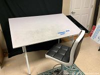 Photo showing the drafting table with chair, tabletop angled and visible wear