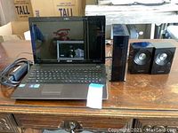 Untested Asus laptop open on a wooden table next to Samsung speakers and power cord.