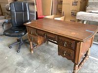 Full view of the carved wooden desk with office chair next to it, showing overall condition and size.