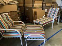 Two white metal patio chairs with multi-colored striped cushions and one ottoman in storage area.