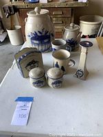 Full set on white table includes large crock, smaller jar, three mugs, salt and pepper shakers, napkin holder, and candlestick holder under soft lighting