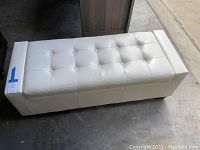 Top and side view of storage bench showing white faux leather upholstery, button tufting, and wear damage on seating area.