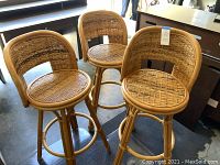 Three wicker and rattan bar stools with rounded backs and circular woven seats, shown in a grouping.