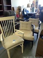 Wide view showing white painted armchair with vertical slats and striped cushion, two barrel chairs with dark wood frames, cream brocade cushions and back pillows