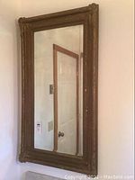 Full view of the antique beveled mirror hanging on a wall, showing the overall shape and ornate wooden frame.