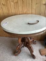 Photo showing the oval marble top table with ornate wooden base and detached piece on top, illustrating overall structure and condition.