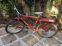 Side view of red Bridgestone bicycle showing full frame, saddle, tires, rear rack, and kickstand.