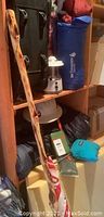 Wide view of camp gear on shelving showing blue tent bag, walking stick, lamp and suitcase.