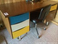 Desk with multicolored drawers alongside the black office chair on caster wheels.