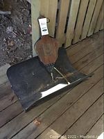Fireplace bellows laying on its side showing black leather bag and curved metal plate base.