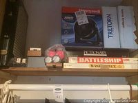 Shelf with boxed board games including Pictionary and Battleship, pink dumbbells, and various boxes including Honeywell and Tretorn.