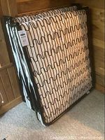 Full view of two folded IKEA SYLLING folding cots with foam mattresses leaning against the wall.