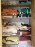 Shelves with multiple folded towels and linens including striped beach towels, solid and patterned bath towels in colors orange, green, cream, beige, and white.