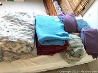 Overview of various folded blankets and linens in different colors and patterns arranged on a bed.