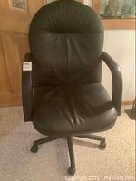 Full view of the black office chair with padded backrest and seat, armrests, and caster wheels under the seat.