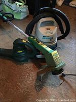 Photo of Shop Vac, Weed Eater trimmer, and Yard Works blower on wooden floor showing the lot contents