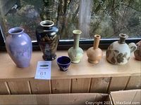 Photo showing six assorted vases and a small blue pottery bowl on a wood window sill.