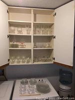 Full view of glassware stored in kitchen cabinet including stemware, etched glasses, plates, punch bowl, salt and pepper shakers.