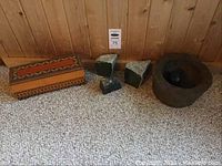 Wooden box, three cut stones and stone mortar displayed on carpet in front of wood panel wall