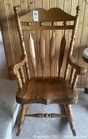 Front view of solid wood rocking chair showing carved backrest with spindled design, armrests, and contoured seat.