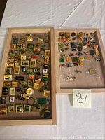 Overview photo showing the extensive collection of advertising pins and key holders laid out in two wooden trays on a white cloth background.