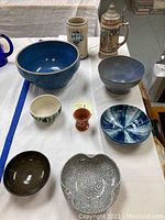 Table displaying various pottery and ceramic items including bowls, mugs, decorative dish, and a stein.