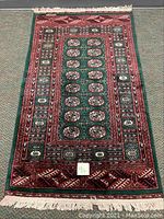 Full length top-down view of the Bokhara oriental rug showing intricate red, green, and beige patterns with fringes at the ends.