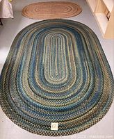 Large oval braided rug featuring blue, green, and beige tones laid out on the floor.