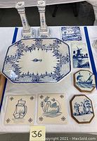 Blue and white ceramic lot including two tall candlesticks, a large rectangular serving platter with floral and scroll pattern, two hexagonal wall plaques with nautical themes, and six square decorative tiles with sailboats and swans.