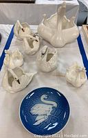 Lot of six white ceramic swan figurines and one blue decorative plate arranged on a table
