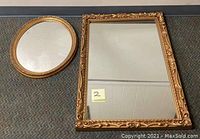Two brass tone mirrors laid flat side by side, showing the round and rectangular shapes with ornate frames