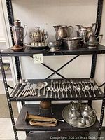 Shelves holding assorted silverplate, pewter, and copper vessels, cutlery, and a copper horn.