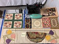 Overview of the lot showing Singer sewing machine, tray with sewing accessories and handmade textiles with floral and geometric patterns.