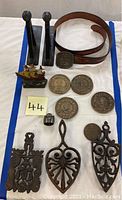 Full view of lot arranged on white cloth showing all items including belt, ship figurine, medallions, ring, cast iron pieces, and black stands.