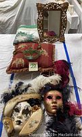 Quilt folded, two Venetian carnival masks on a red throw pillow with elephant design, small ornate brass-tone mirror in background