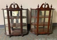 Front view of the pair of wooden wall curio cabinets with glass doors and curved glass sides