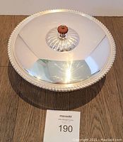 Close-up view of serving dish lid with orange pumpkin-shaped knob, highlighting reflective surface and ribbed detailing.